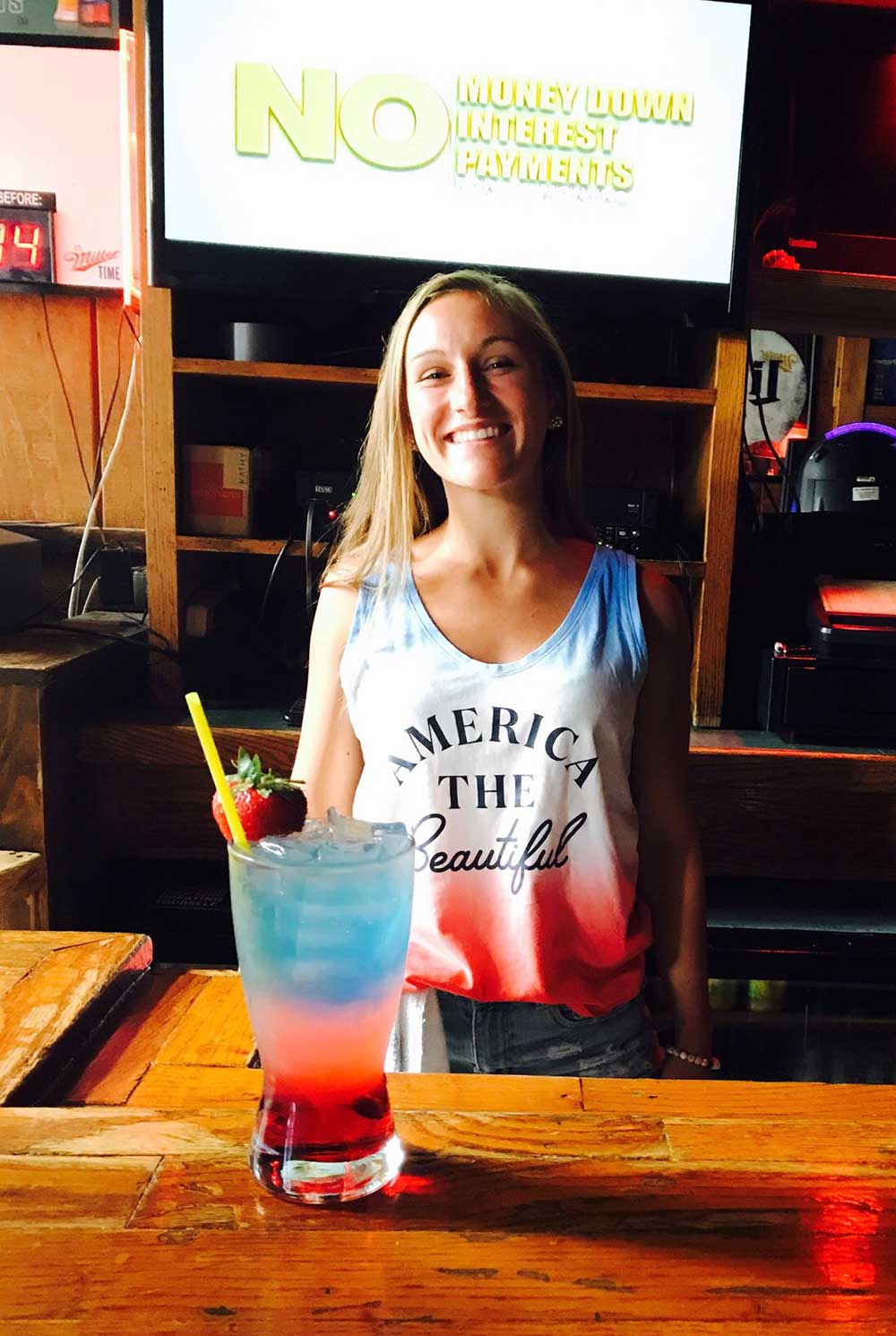photo of bartender wearing a USA shirt with a USA-looking drink in front of her
